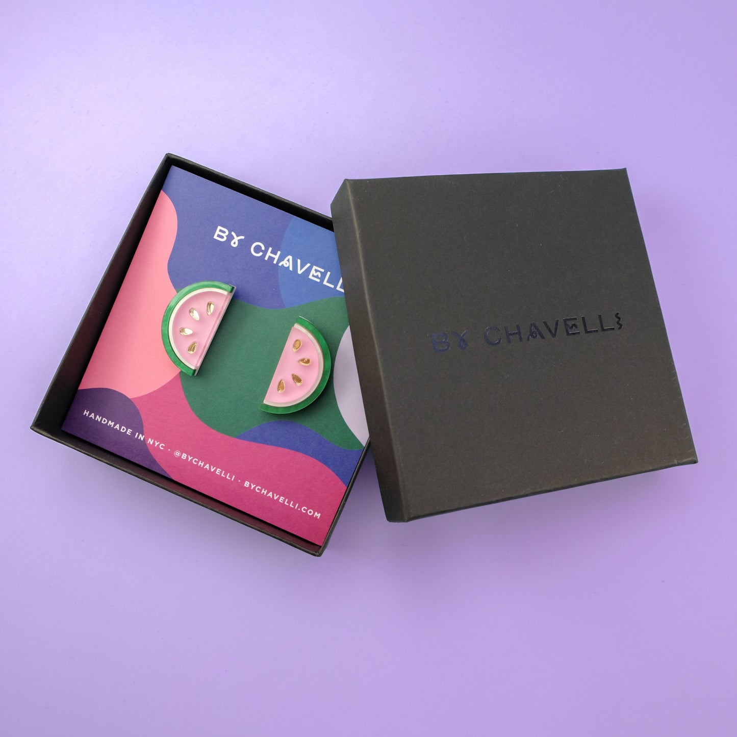 Watermelon slice stud earrings in gift box, glossy bubblegum-pink centers, marbled emerald-green rinds, crisp white stripes, tiny gleaming gold seeds, playful presentation card #color_pink_green