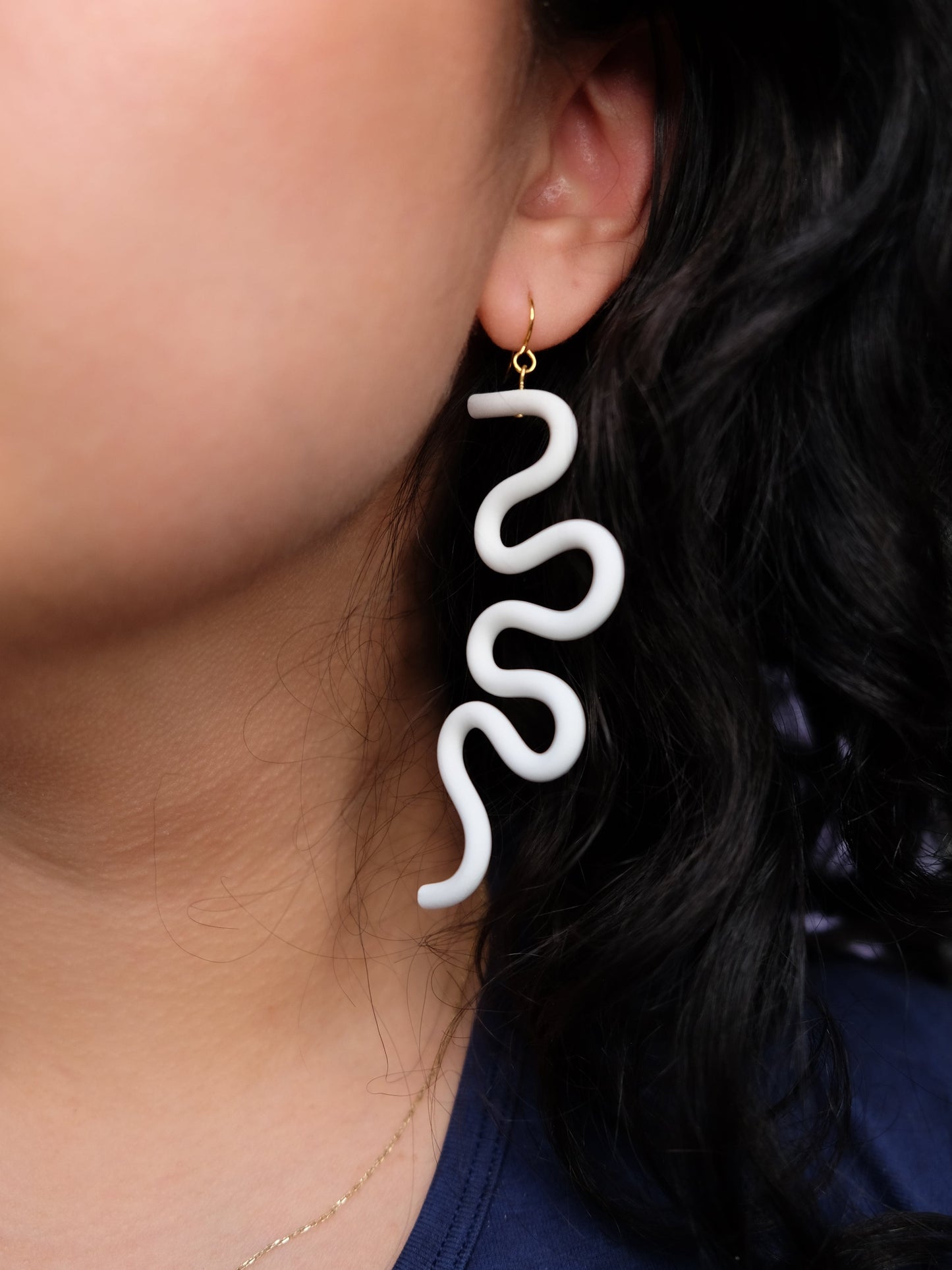 White wavy earring, bold, lightweight, drop-length, smooth finish, worn by a person with dark hair #color_white