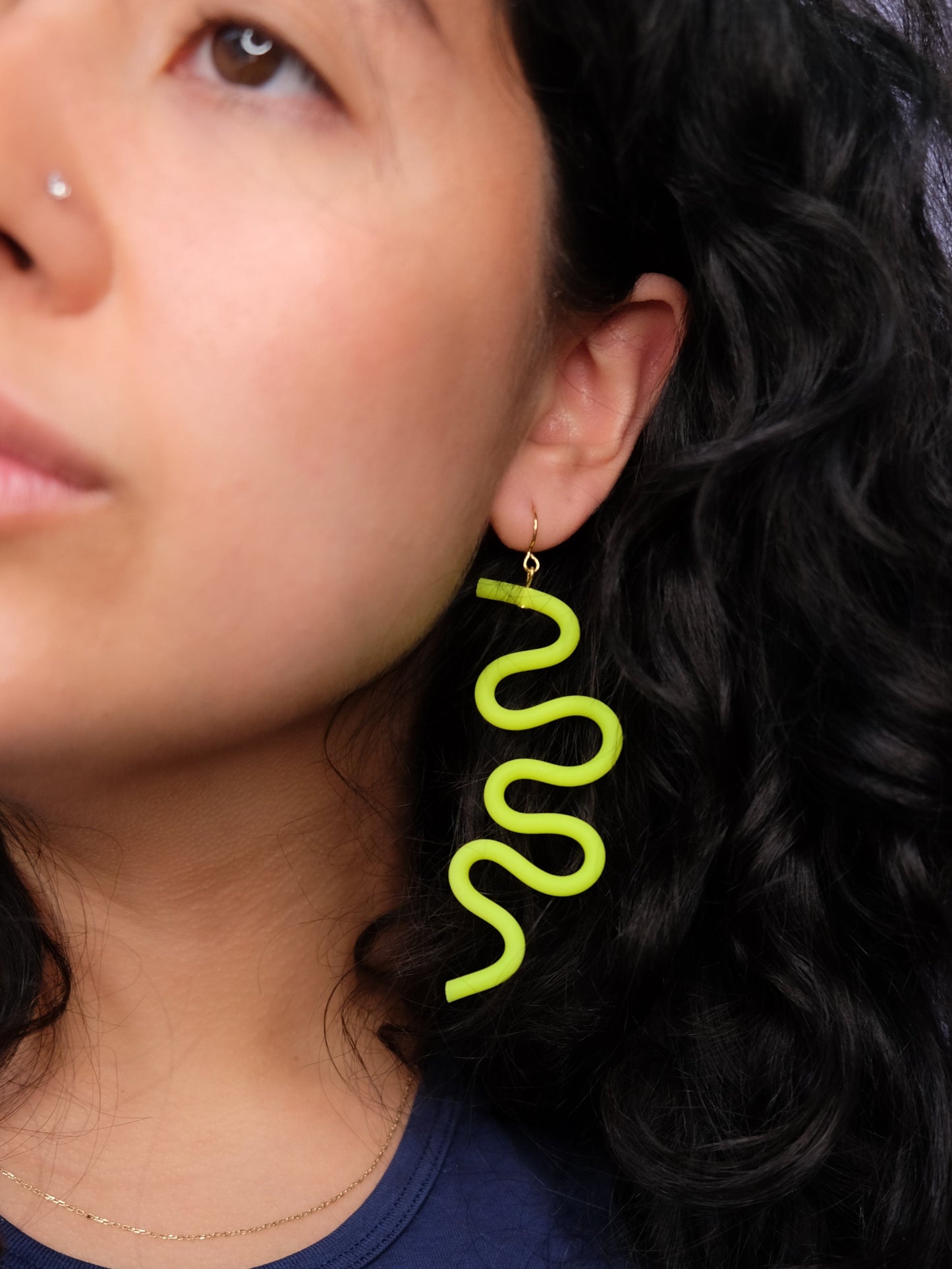 Neon-green wavy earring, oversized, matte, tubular, sculptural, worn by a person with dark hair #color_neon-green
